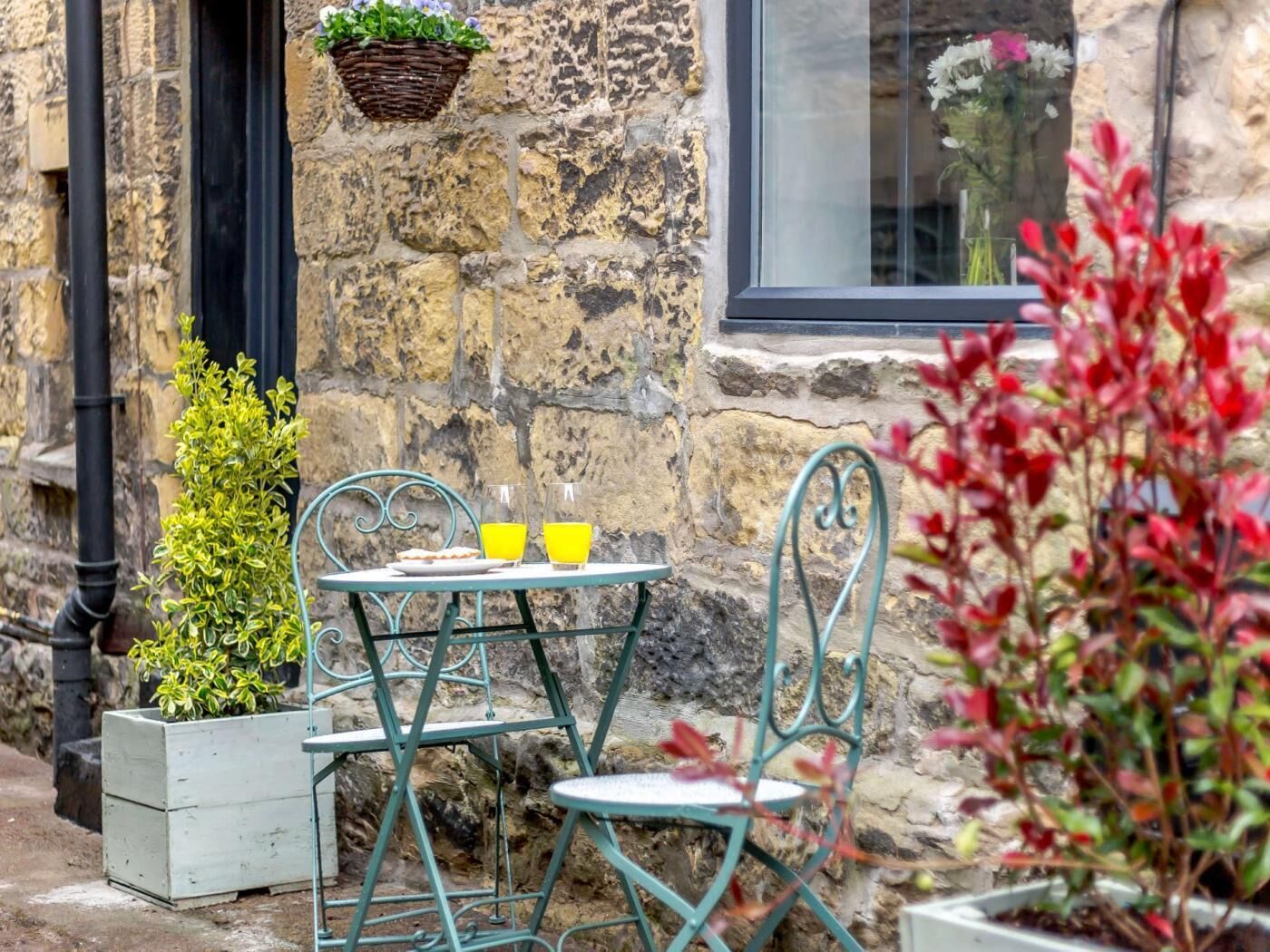 A stone building with a window, a table with chairs, and potted plants.