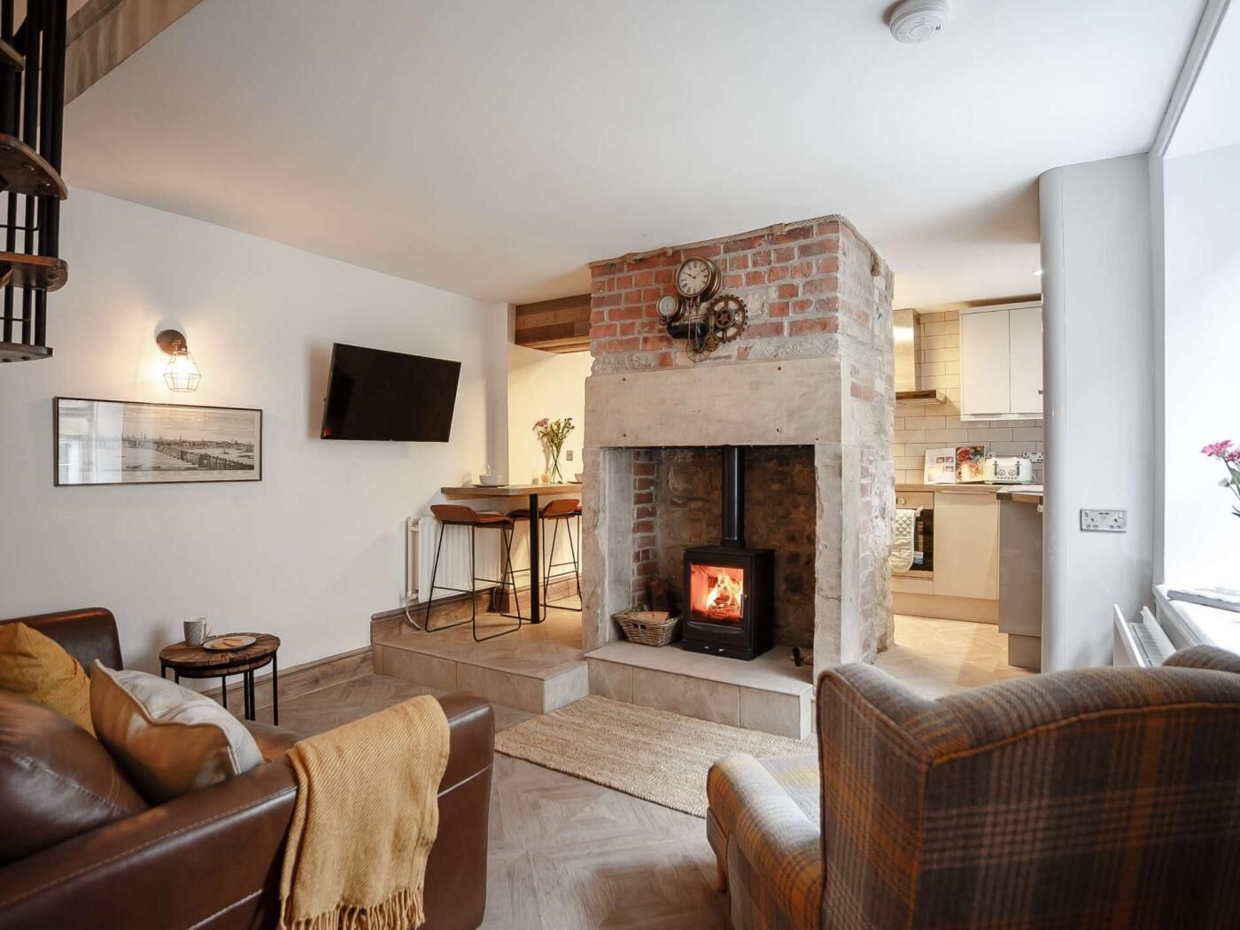 A living room with a fireplace, a TV mounted on the wall, and a kitchen area visible through an open door.