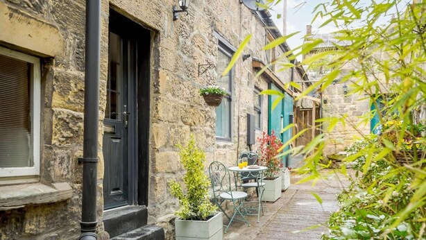 A stone building with a black door, outdoor seating, and potted plants. - 2 Bed in Morpeth (oc-82238) (Rothbury)