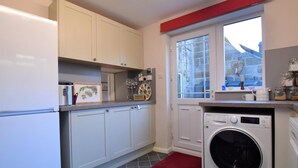 A compact kitchen with white cabinets, a washing machine, and a window with a view.