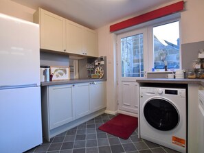 A compact kitchen with white cabinets, a washing machine, and a window with a view.