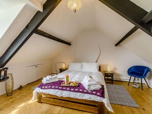 A bedroom with a sloped ceiling, a wooden bed, a blue chair, and a radiator.