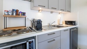 A modern kitchen with a stove, microwave, sink, and a shelf with various containers. - 1 bedroom accommodation in Oostduinkerke (Oostduinkerke)