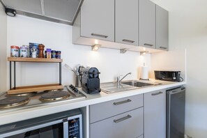 A modern kitchen with a stove, microwave, sink, and a shelf with various containers. - 1 bedroom accommodation in Oostduinkerke (Oostduinkerke)