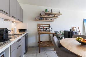 A modern kitchen with a microwave, toaster, and sink. There is a wooden table with a bowl of fruit and a chair. - 1 bedroom accommodation in Oostduinkerke (Oostduinkerke)