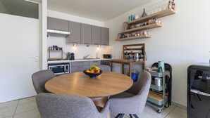 A modern kitchen with grey cabinets, a wooden dining table with four chairs, and a fruit bowl. - 1 bedroom accommodation in Oostduinkerke (Oostduinkerke)