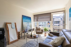 A living room with a sofa, armchair, coffee table, and artwork on the wall. - 1 bedroom accommodation in Oostduinkerke (Oostduinkerke)