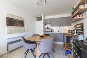 A modern kitchen with grey cabinets, a dining table with grey chairs, and a fruit bowl. - 1 bedroom accommodation in Oostduinkerke (Oostduinkerke)