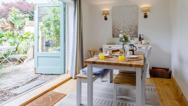 A modern dining area with a wooden table, chairs, and a view through a glass door to a garden. - 1 Bed in Chulmleigh (oc-82389) (Chulmleigh)