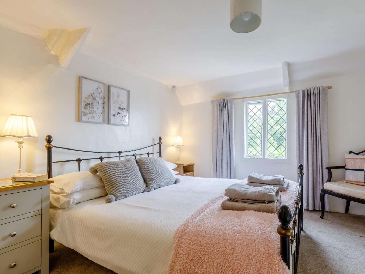 Une chambre à coucher comprenant un lit, des tables de chevet, une chaise, une fenêtre avec des rideaux et des œuvres d’art murales.
