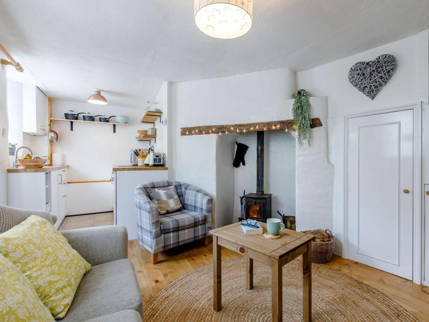 A cozy living room with a fireplace, a sofa, a table, and a kitchen area with shelves.