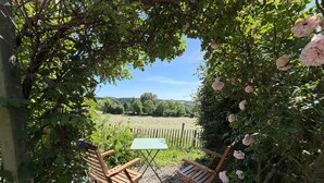 Un jardí amb taula i dues cadires, envoltat de verdura i vista a un camp.