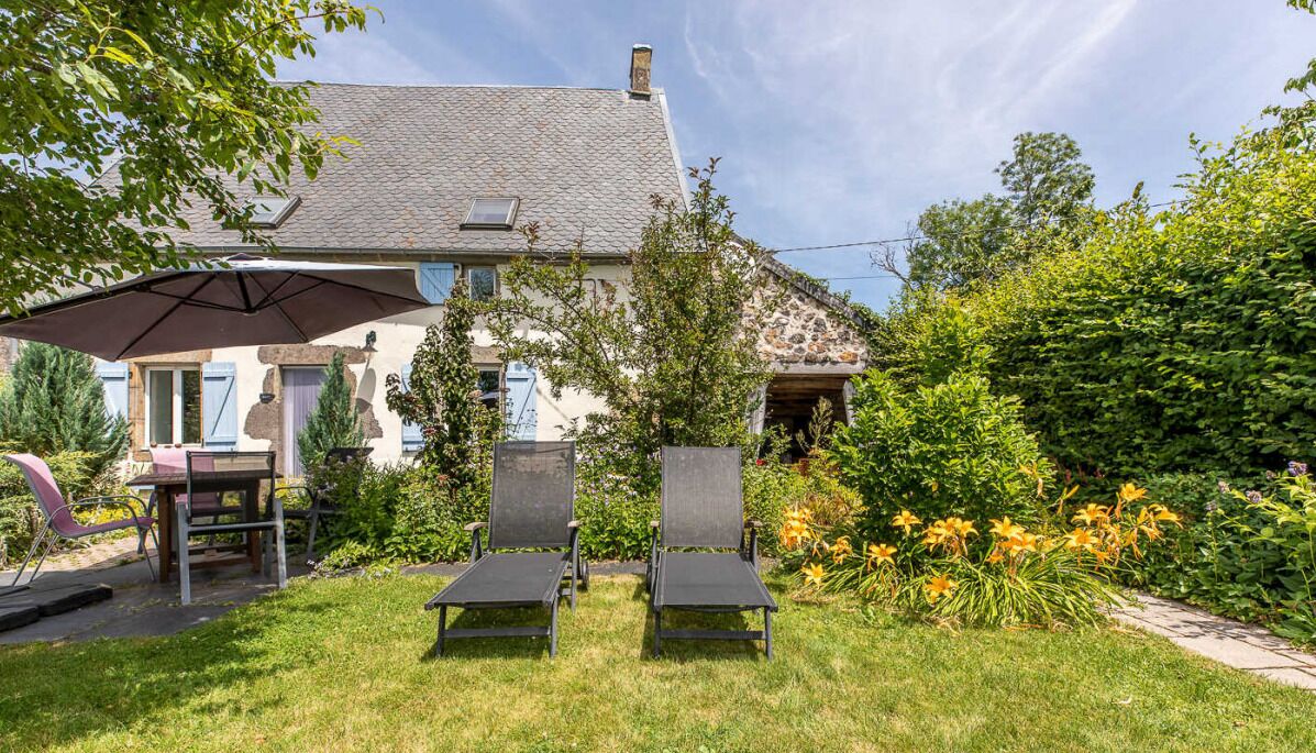 A house with a garden, outdoor seating, and a patio umbrella.