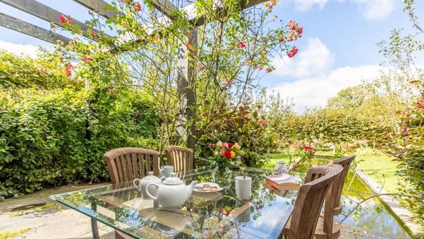 Ein Glastisch mit Stühlen, eine weiße Teekanne und ein Teller Essen in einem Garten.