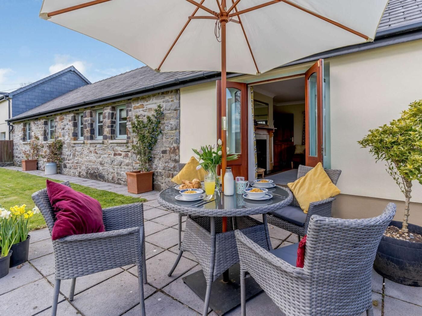 A patio with wicker furniture, a table set for breakfast, and a stone building in the background.
