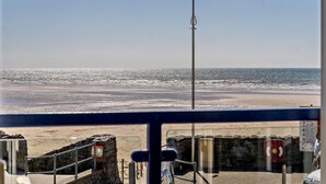 Blick auf einen Strand mit einer Fahne an einem Mast, einer Steinmauer und einem Schild.
