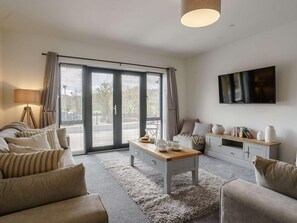 Ein modernes Wohnzimmer mit einer Couch, einem Couchtisch, einem Fernseher und einer Glastür zum Außenbereich.