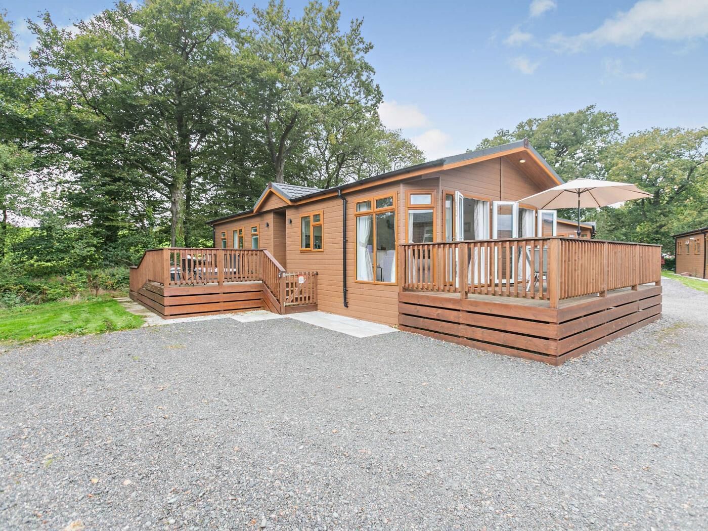 Une cabane en bois dotée d’une terrasse, d’un patio couvert et d’une allée en gravier.