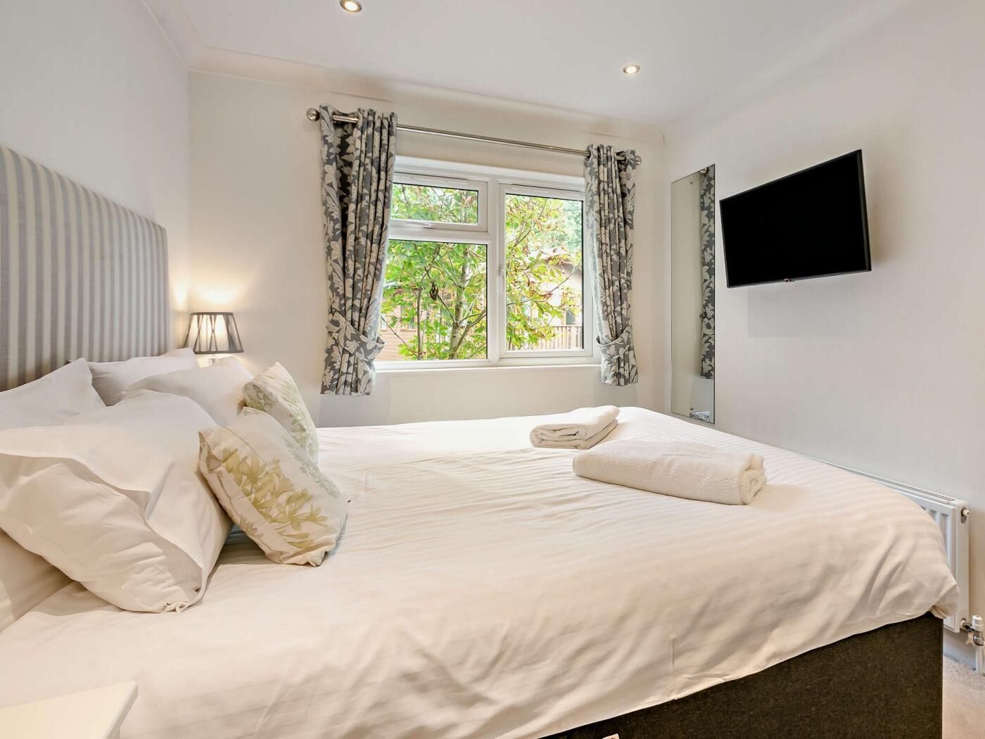 Une chambre d’hôtel avec un lit, une télévision, une fenêtre avec des rideaux et un radiateur.