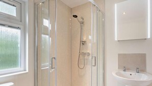 A modern bathroom with a glass-enclosed shower, a white sink, and a large window.