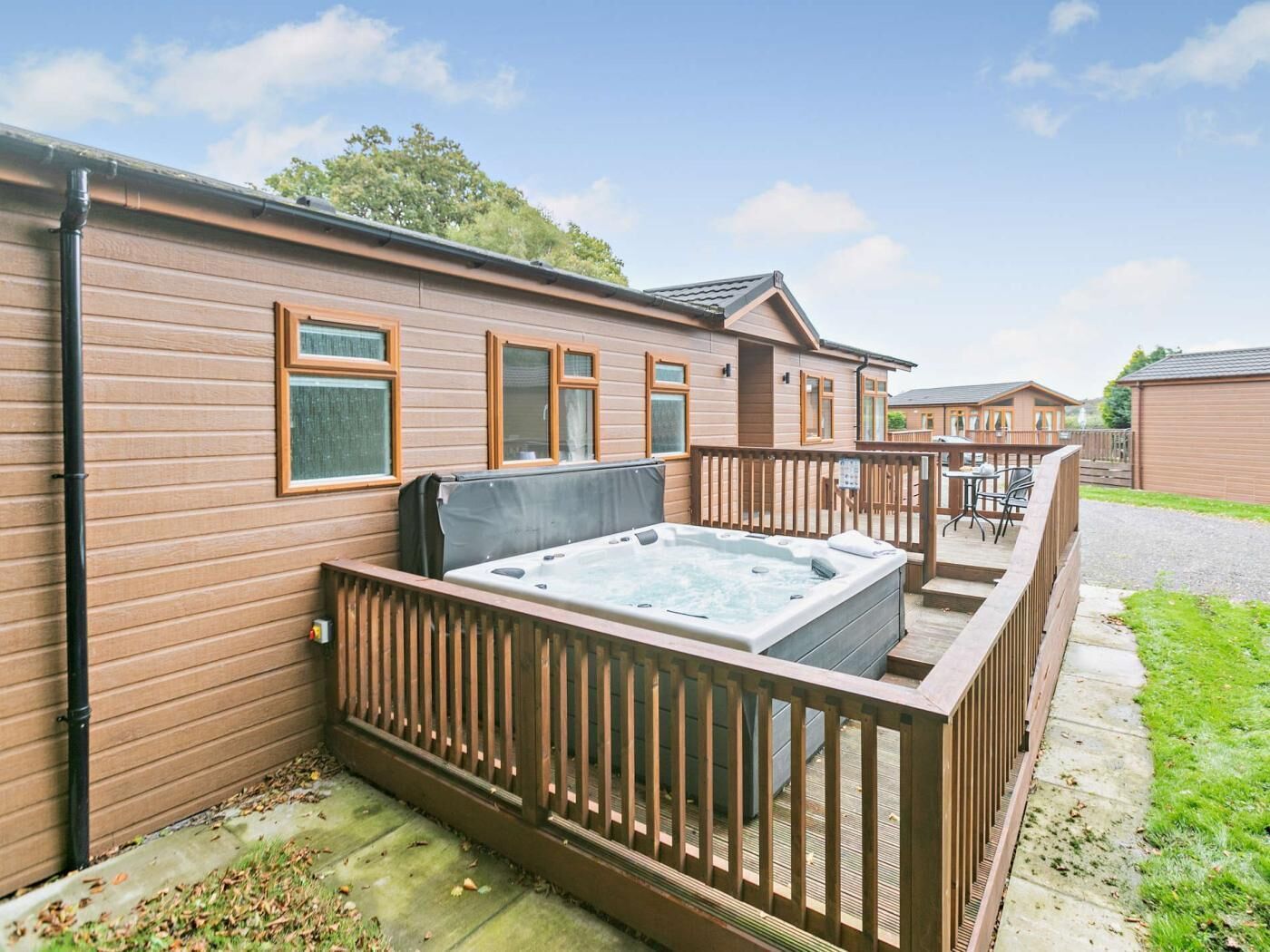 A caravan with a hot tub, wooden deck, and a fenced patio area.