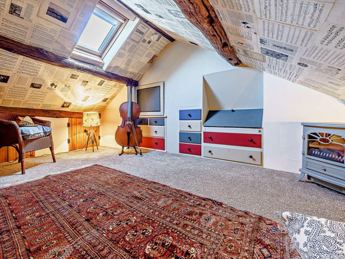 Een kamer met een schuine kap, een cello, een bed, een vloerkleed en een ladekast.
