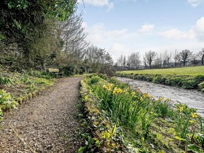 A gravel path alongside a river with yellow flowers and trees in the background. - 1 Bed in Ulverston (oc-82447) (Gleaston)