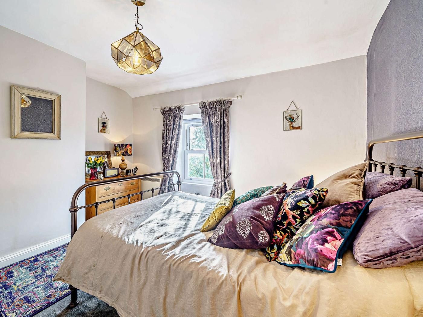 A bedroom with a bed, a bedside table, a hanging light fixture, and a window with curtains.