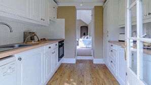 Een smalle keuken met witte kasten, een houten aanrechtblad en uitzicht op een slaapkamer door een open deur.