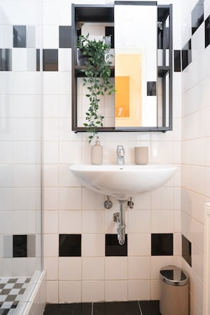 Ein Badezimmer mit Waschbecken, Spiegel, Topfpflanze und Mülleimer.