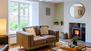 Ein gemütliches Wohnzimmer mit einer Couch, einem Kamin, einem großen Fenster und einem Spiegel.