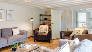Ein modernes Wohnzimmer mit einer Couch, Sesseln, einem Couchtisch und einem Bücherregal.
