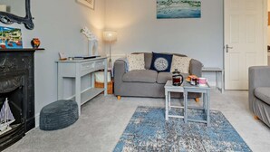 Uma sala de estar aconchegante com lareira, sofá, mesa de centro e um quadro na parede.