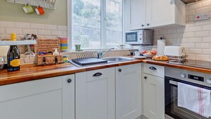 Uma cozinha com armários brancos, micro-ondas, torradeira, pia e janela com persianas.
