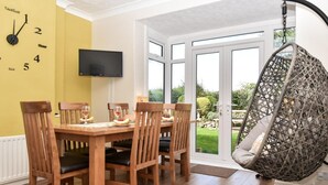 Un coin repas avec une table et des chaises en bois, un téléviseur fixé au mur et un fauteuil suspendu.
