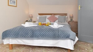 Un lit bien fait, recouvert d’une couverture bleue matelassée, avec des oreillers et une table de chevet sur laquelle se trouvent une lampe et un plateau contenant des éléments pour le petit-déjeuner.