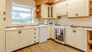 Une cuisine avec des meubles blancs, un four à micro-ondes, un four traditionnel et une fenêtre donnant sur un paysage verdoyant.