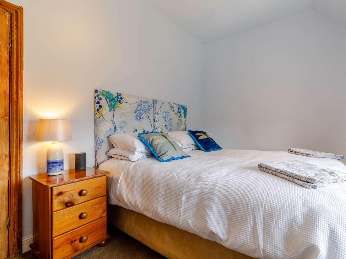 A bedroom with a bed, a nightstand, a lamp, and a dresser.