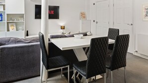 A modern dining area with a white table and black chairs, a white pillar, and a wall-mounted TV. - Modern Edinburgh City Escape | Sleeps 2 (Edinburgh)