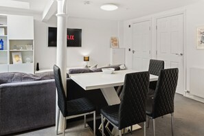 A modern dining area with a white table and black chairs, a white pillar, and a wall-mounted TV. - Modern Edinburgh City Escape | Sleeps 2 (Edinburgh)