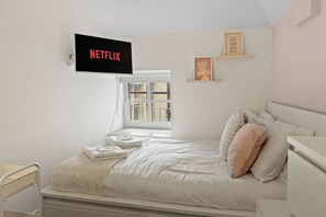 A bedroom with a bed, a TV mounted on the wall displaying 'NETFLIX', a window, and a shelf with decorative items. - Modern Edinburgh City Escape | Sleeps 2 (Edinburgh)