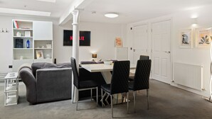 A modern living room with a sofa, a dining table with chairs, a bookshelf, and a flat-screen TV displaying the Netflix logo. - Modern Edinburgh City Escape | Sleeps 2 (Edinburgh)