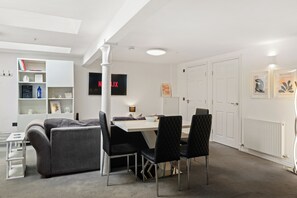 A modern living room with a sofa, a dining table with chairs, a bookshelf, and a flat-screen TV displaying the Netflix logo. - Modern Edinburgh City Escape | Sleeps 2 (Edinburgh)