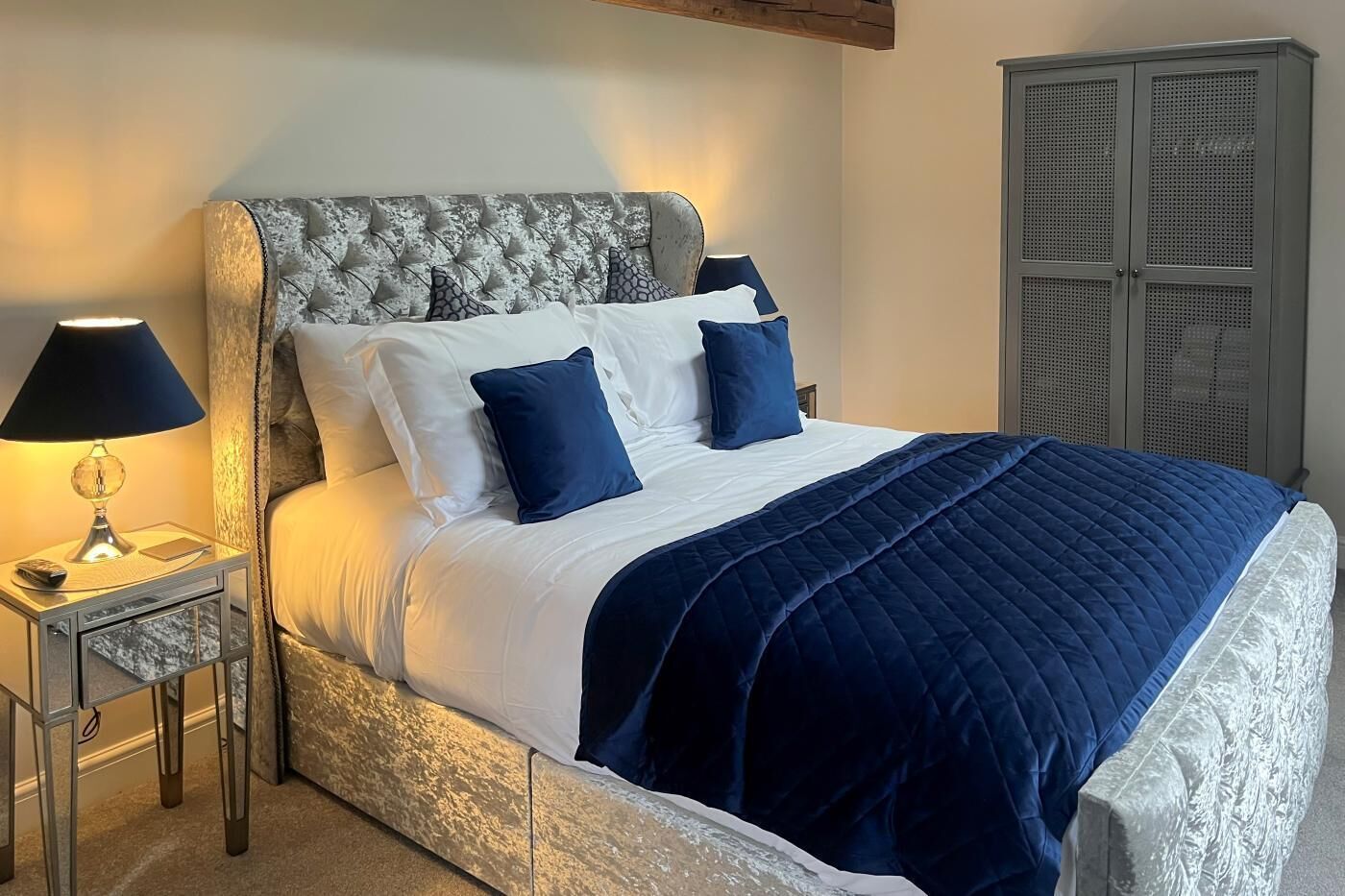 A bed with a tufted headboard, a bedside table with a lamp, and a wardrobe.