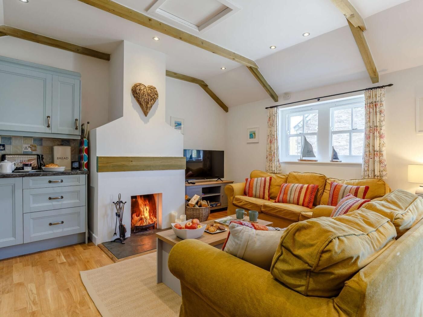A cozy living room with a fireplace, a sofa, a television, and a kitchen area with cabinets and a countertop.