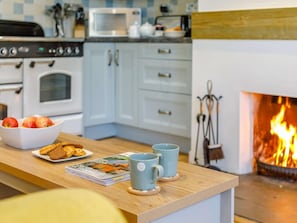 A kitchen with a fireplace, a table with apples, bread, and a magazine, and a microwave above the oven. - 2 Bed in Wadebridge (oc-82681) (Little Petherick)