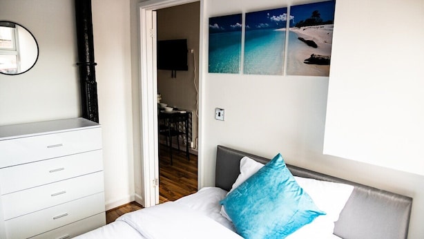 Een slaapkamer met een bed, een dressoir, een televisie en een muur met een strandafbeelding.