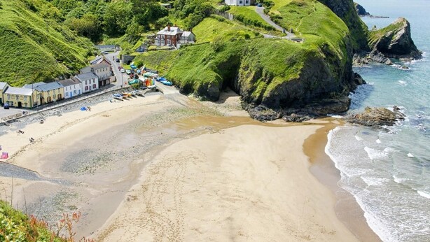 A coastal town with a sandy beach, a prominent white building on a cliff, and a road leading to the beach. - 4 Bed in Cardigan (oc-82766) (Rhos-hill)