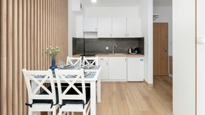 A modern kitchen with white cabinets, a wooden countertop, and a dining area with white chairs and a blue tablecloth. - Cozy Studio with a Balcony | Parking (Grzybowo)