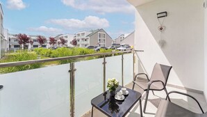 A balcony with a glass railing, a table with two chairs, a small plant, and a wall-mounted light fixture. - Cozy Studio with a Balcony | Parking (Grzybowo)